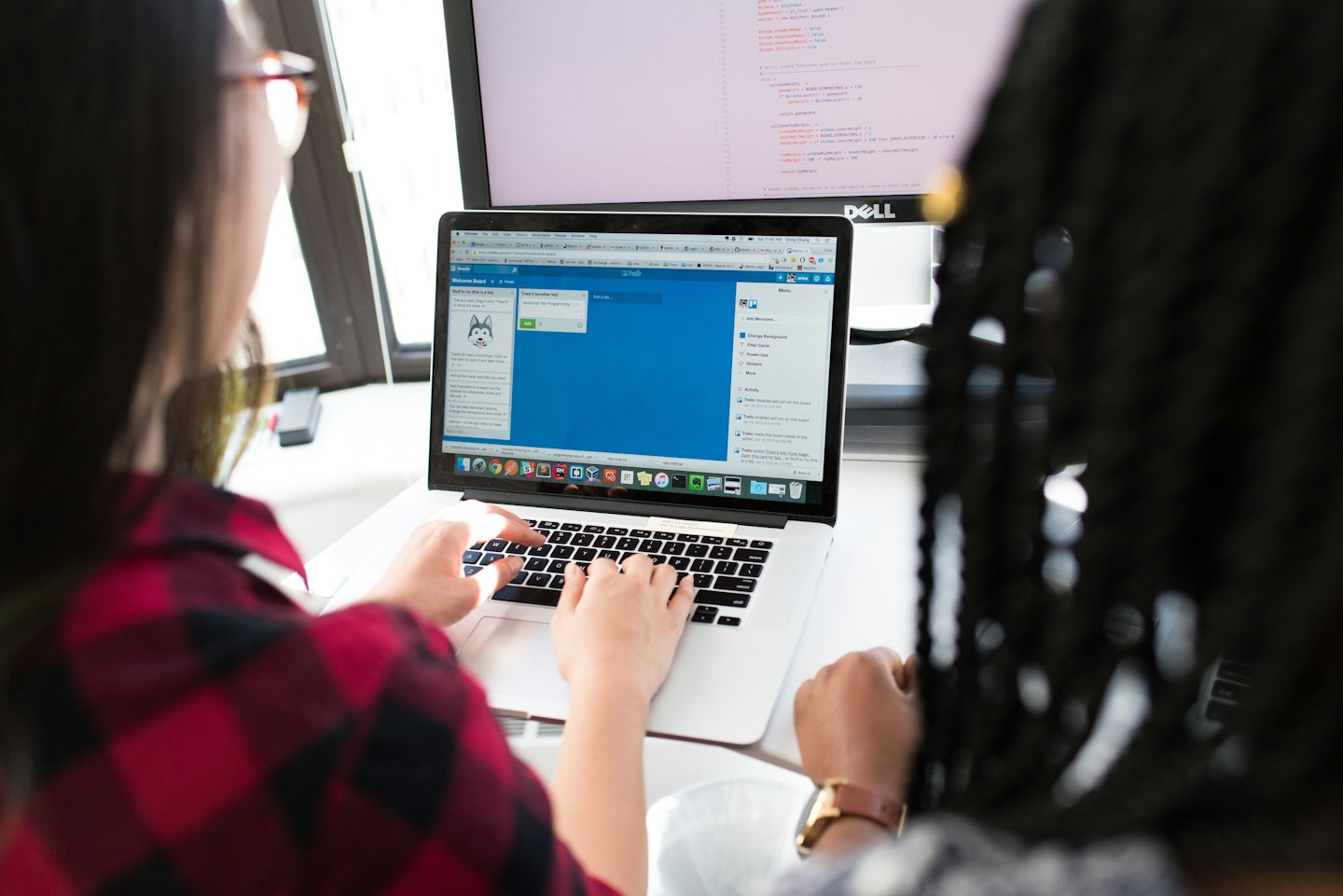 Dua rekan kerja berkolaborasi di laptop menggunakan Trello.