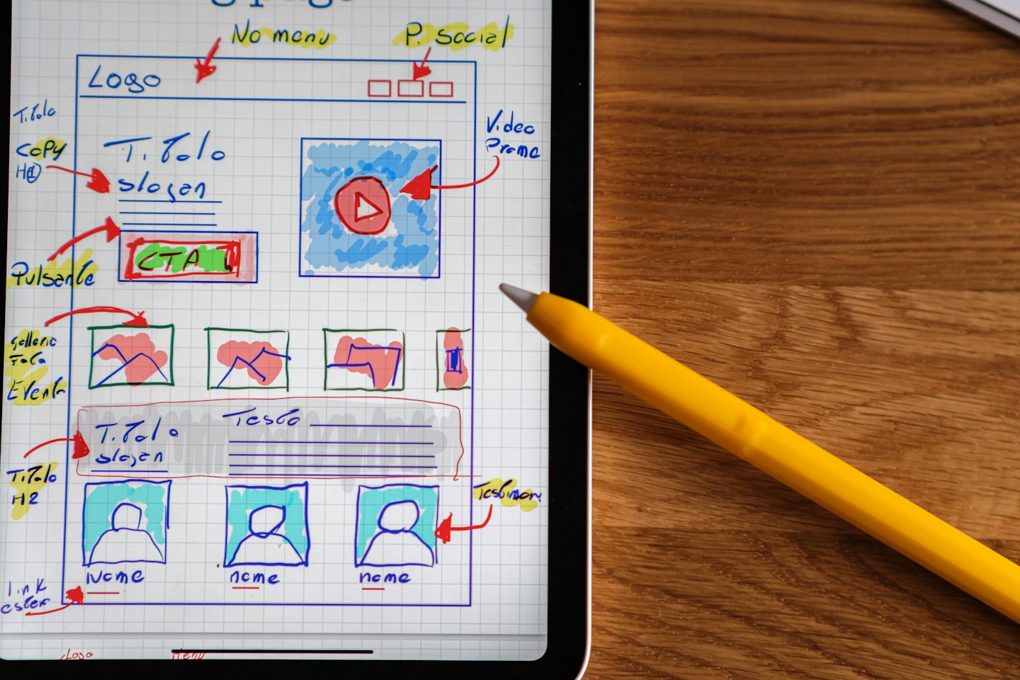Sketsa rancangan situs web ditampilkan di tablet digital di atas meja kayu.