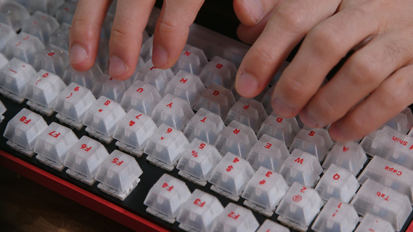 Tangan mengetik di keyboard mekanik merah dan hitam dengan tombol putih.