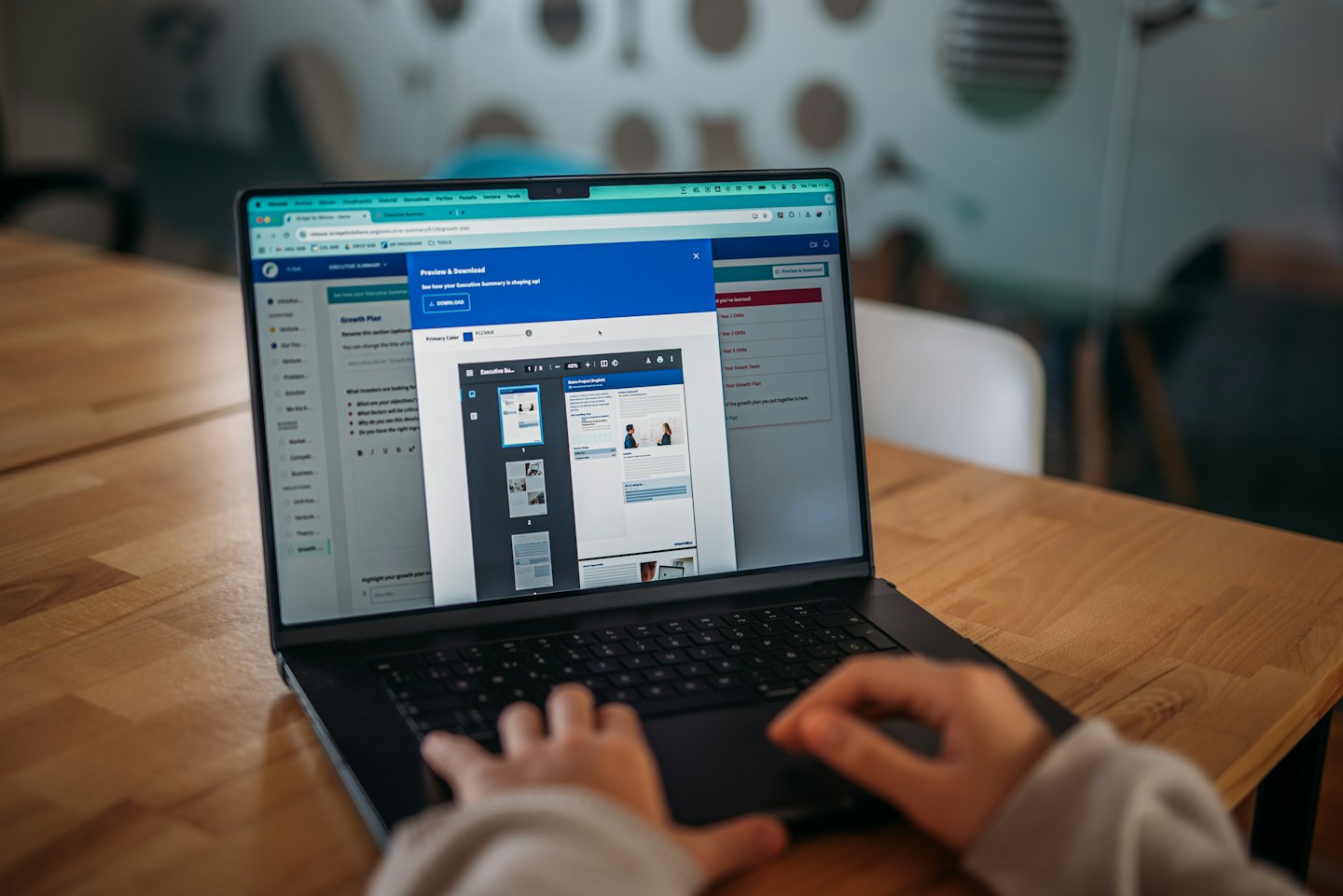 Tangan mengetik di laptop menampilkan pratinjau dokumen.